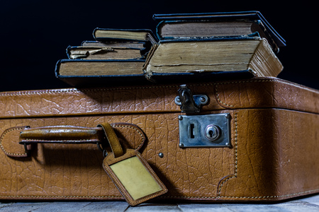Old stylish suitcase. Old books in a suitcase. Suitcase on a wooden table. Black backgroundの写真素材
