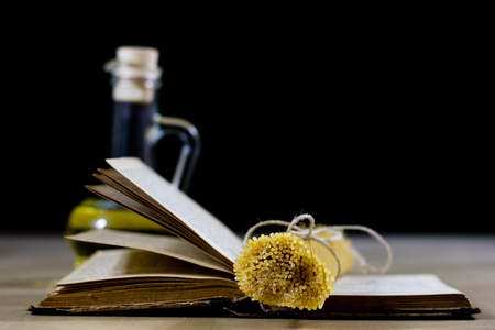 Pasta and olive oil on an old kitchen table. Recipes in old books in the kitchen on a wooden table. Black background.の写真素材
