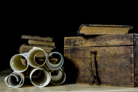 Old rolls and plans in folded paper rolls. Old book and case. Documents on an old wooden table. Black background.の写真素材