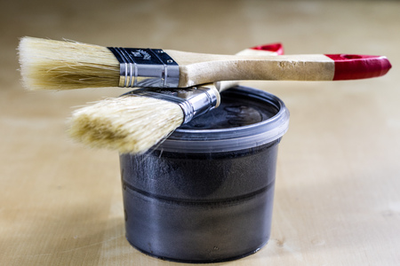 Pedzel for painting with oil paint on a wooden workshop table and a can of paint. A bristle brush in a workshop. Black backgroundの写真素材