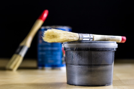Pedzel for painting with oil paint on a wooden workshop table and a can of paint. A bristle brush in a workshop. Black backgroundの写真素材