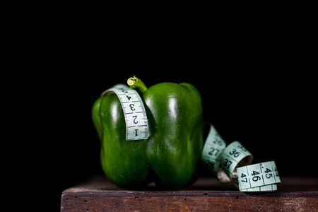 Tasty paprika on an old dark wooden table. A tailor measuring tape next to the vegetable. Vegetables on a diet. Black backgroundの写真素材