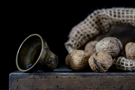 Nuts in a natural bag. A bag of nuts and a bell on an old dark wooden table. Black background