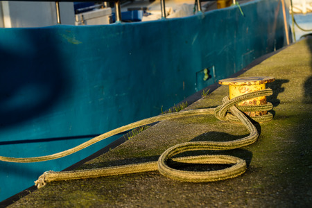 Bollard in the fishing port on the wharf. The wrapped rope mooring fishing boats in the sea port....