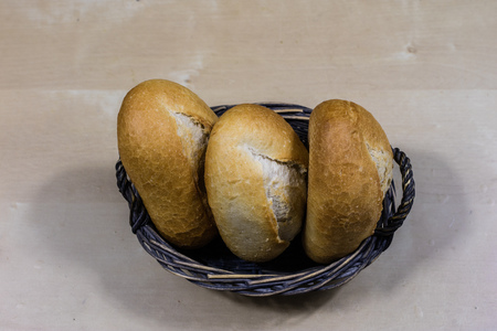 Tasty fresh bread in a wicker basket. Rolls in a basket on a wooden kitchen table. Black background.