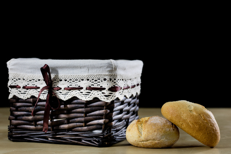 Tasty fresh bread in a wicker basket. Rolls in a basket on a wooden kitchen table. Black background.の写真素材