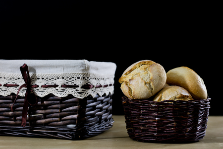 Tasty fresh bread in a wicker basket. Rolls in a basket on a wooden kitchen table. Black background.の写真素材