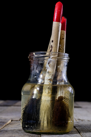 Painting pedzels soaked in water on a wooden workshop table. Painting accessories. Black background.の写真素材