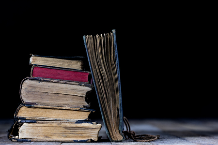 Old destroyed books on a wooden table. Reading room library with very old books on a wooden table. Black background.の写真素材