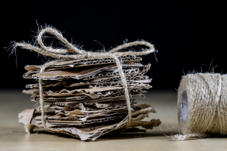 Cardboard pieces stacked and tied with a jute string. Waste paper packed in cubes and tied with a string. Black background.の写真素材