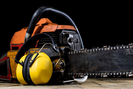 An old power saw for cutting wood. Chainsaw and protective clothing on a wooden workshop table. Black background.の写真素材