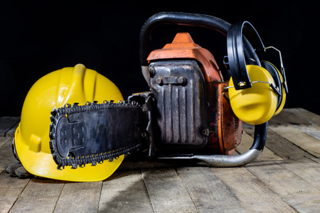An old power saw for cutting wood. Chainsaw and protective clothing on a wooden workshop table. Black background.の写真素材