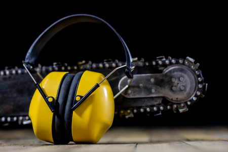 An old power saw for cutting wood. Chainsaw and protective clothing on a wooden workshop table. Black background.の写真素材