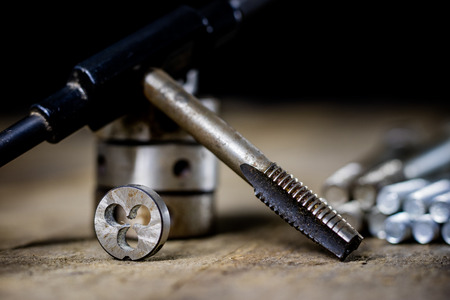 Metalwork tools on the workshop table. Threading dies and taps in an old dusty workshop. Black background.の写真素材