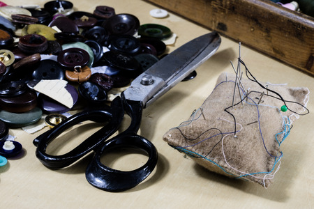 Garment accessories spread on a light wooden table. Threads, scissors and sewing needles in a...