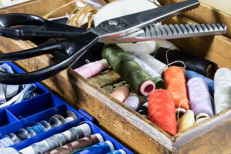 Garment accessories spread on a light wooden table. Threads, scissors and sewing needles in a...