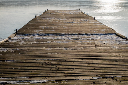 Fishing pier on a frozen lake. Bridge for mooring fishing boats and ice on the lake. Season winter.の写真素材