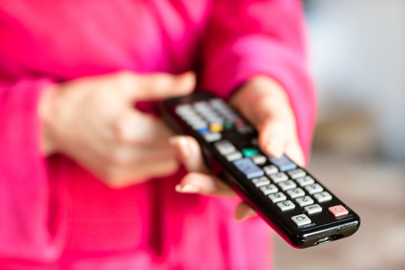 TV remote control held in women's hands. Switching channels on the TV with the remote control. Time of the day, morning.の写真素材