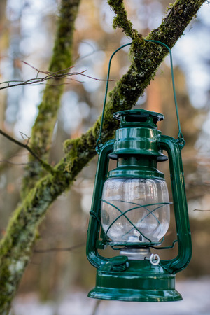 Oil lamp suspended on a branch in the forest. Old traditional lighting by the forest path. Winter season.の写真素材