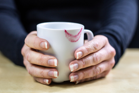 Empty white mug with gloves. Hands in warm gloves holding a china mug on a wooden kitchen table. Light background.の写真素材