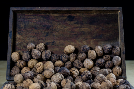 Walnuts on a wooden kitchen table. Nuts and a black wooden crate with a nutcracker. Black background.の写真素材