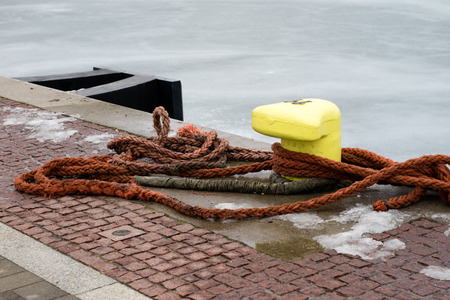 A mooring bollard entwined with a mooring rope. Moored ships at the port quay. Season winter.の写真素材