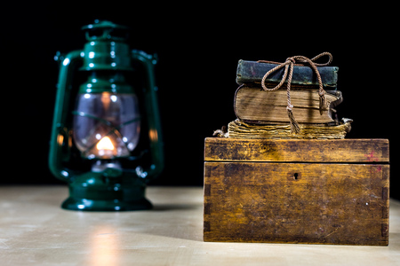 Old oil lamp and books lying on the table. A flame from an old source of light illuminating old prints. Black background.の写真素材
