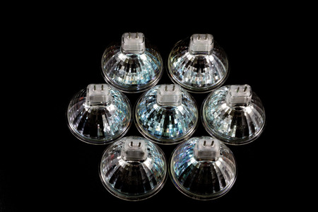 Halogen bulb in a reflective shade. Lighting accessories on a dark tole. Black background.