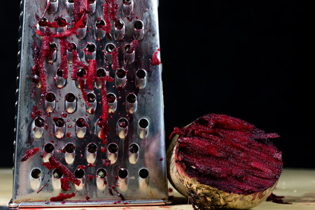 Beet grated on a kitchen grater. Kitchen countertop and preparation of salads. Dark background.の写真素材