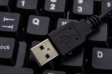 A black computer keyboard and an enlarged USB port. Computer accessories. Dark background.