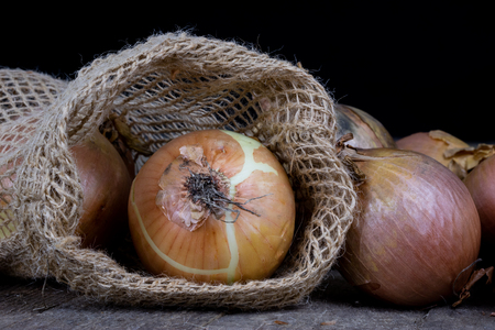 Tasty ripe onion in a jute sack. Vegetables hollowed out in the garden on an old wooden table. Dark background.の写真素材