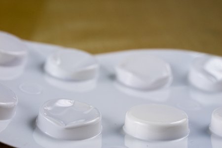 Pills in a wrapper on a wooden table. A medicine for a cold and a headache in a plastic package. Light background.の写真素材