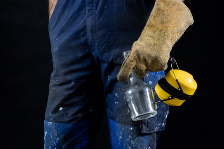 Drunkenness at work. Protective accessories and an empty bottle kept by an employee. Dark background.の写真素材