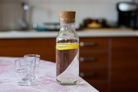 Fresh water with lemon. A refreshing drink in a glass container standing in the kitchen. Interior of a residential home.の写真素材