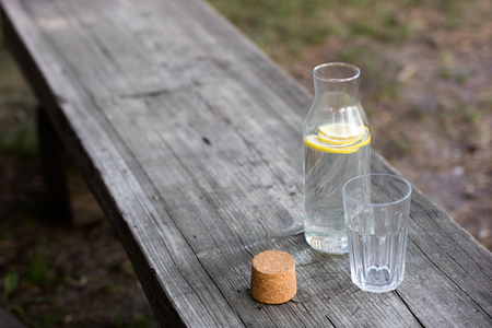 A bottle of water with lemon and a glass. A bench on which a refreshing drink is placed. Season of...