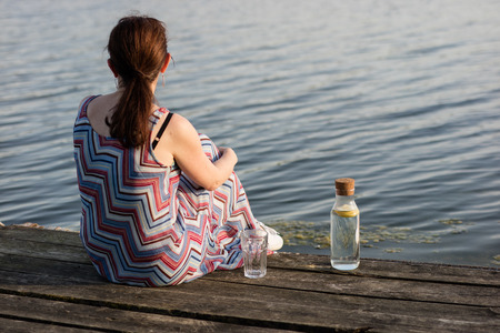 A bottle of water with lemon and a glass. Bridge over the lake and woman. Season of the spring.の写真素材