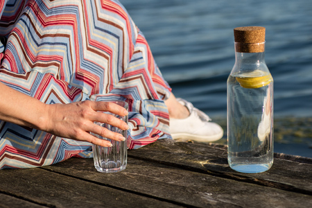 A bottle of water with lemon and a glass. Bridge over the lake and woman. Season of the spring.の写真素材