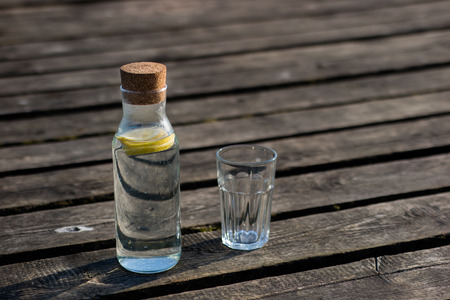 A bottle of water with lemon and a glass. Bridge on which stands a refreshing drink. Season of the spring.の写真素材
