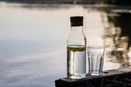 A bottle of water with lemon and a glass. Bridge on which stands a refreshing drink. Season of the spring.の写真素材