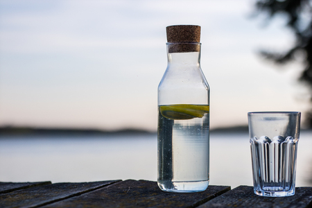 A bottle of water with lemon and a glass. Bridge on which stands a refreshing drink. Season of the spring.の写真素材