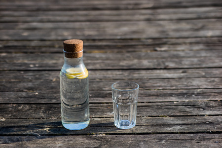 A bottle of water with lemon and a glass. Bridge on which stands a refreshing drink. Season of the spring.の写真素材