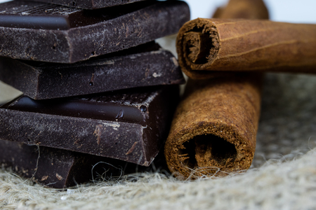 Chocolate in cubes and cinnamon arranged on the kitchen table. Sweet dessert on a linen napkin. Autumn background.の写真素材