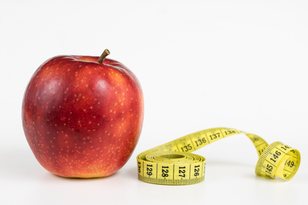 Red apples and a measure of tailor on a white table. Ripe fruits and a tailor's centimeter. White background.の写真素材