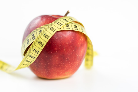 Red apples and a measure of tailor on a white table. Ripe fruits and a tailor's centimeter. White background.の写真素材