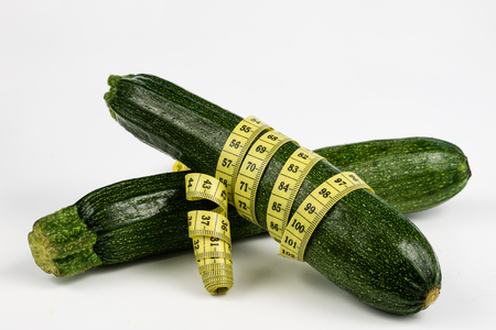 Zucchini on a white table. Tailor measure to measure the waist circumference during the diet. Light background.の写真素材