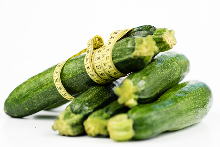 Zucchini on a white table. Tailor measure to measure the waist circumference during the diet. Light background.の写真素材