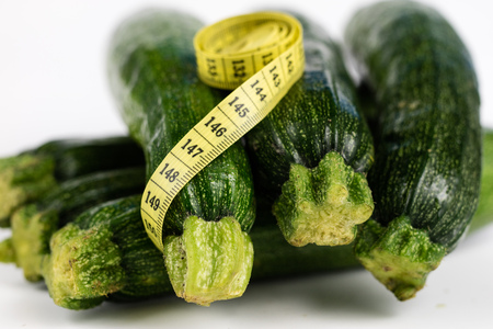 Zucchini on a white table. Tailor measure to measure the waist circumference during the diet. Light background.の写真素材