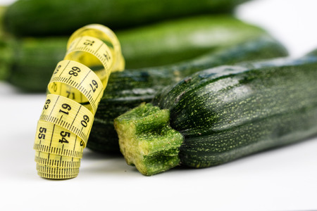 Zucchini on a white table. Tailor measure to measure the waist circumference during the diet. Light background.の写真素材