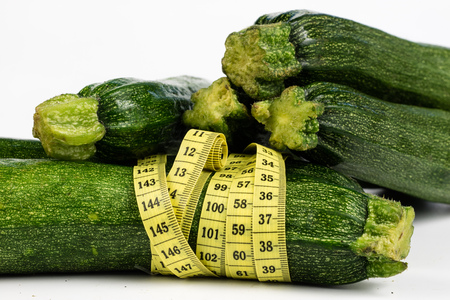 Zucchini on a white table. Tailor measure to measure the waist circumference during the diet. Light background.の写真素材