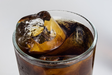 Cold drink with ice in a glass on a white table. A way to cool down on hot days. White background.